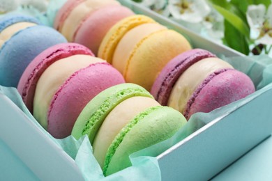 Photo of Many delicious colorful macarons in box on light blue background, closeup