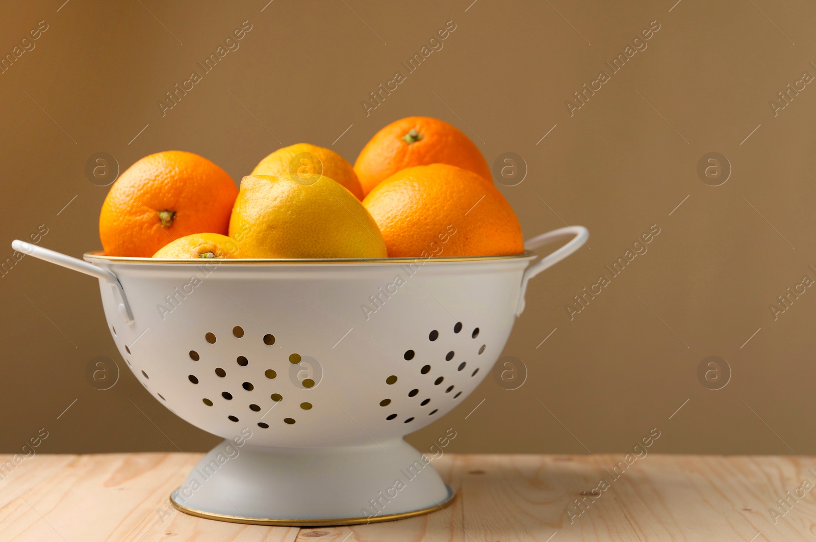 Photo of Colander with fresh citrus fruits on wooden table, space for text