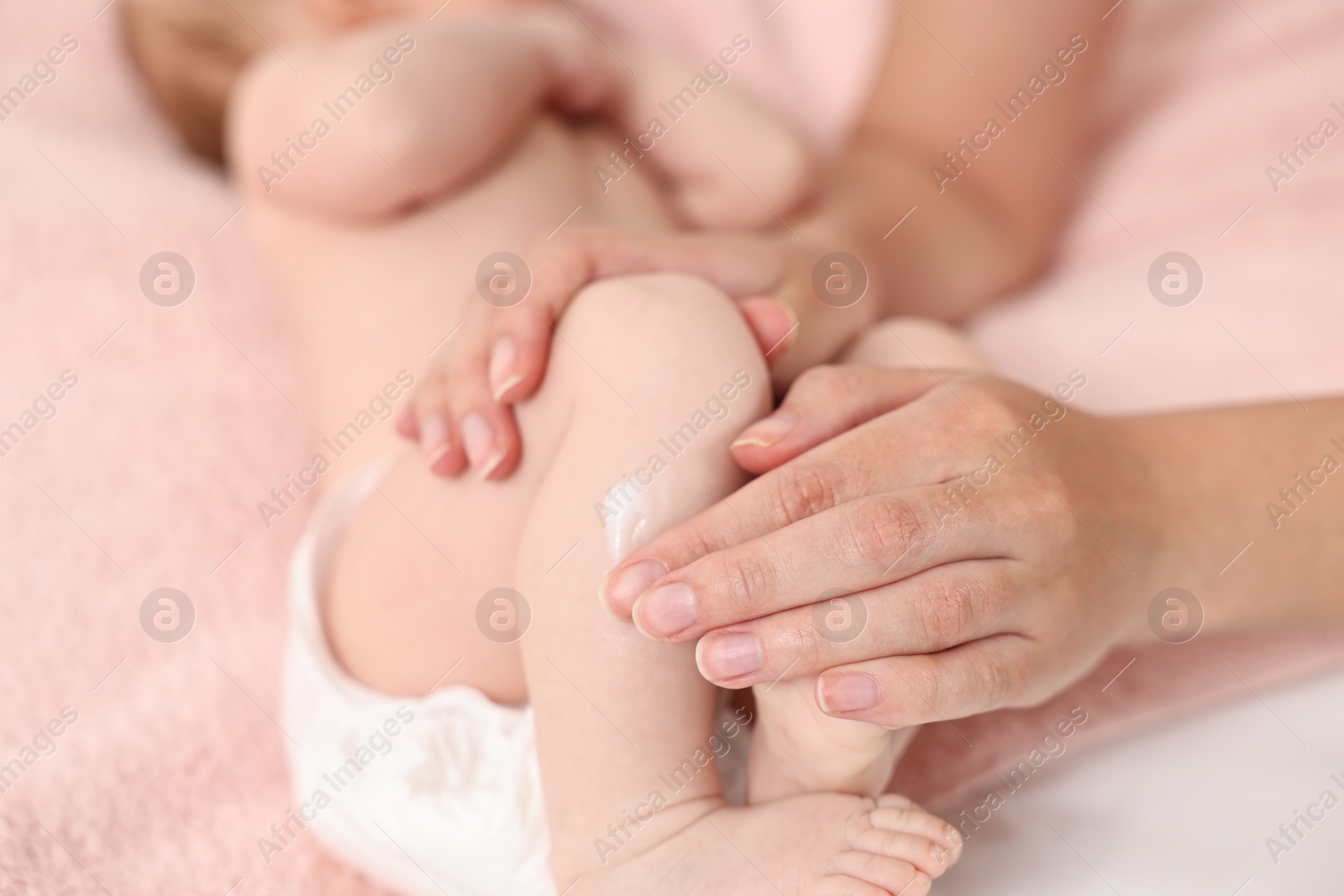 Photo of Woman applying body cream onto baby`s skin on bed, closeup