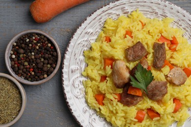 Photo of Delicious pilaf with meat and ingredients on grey wooden table, flat lay