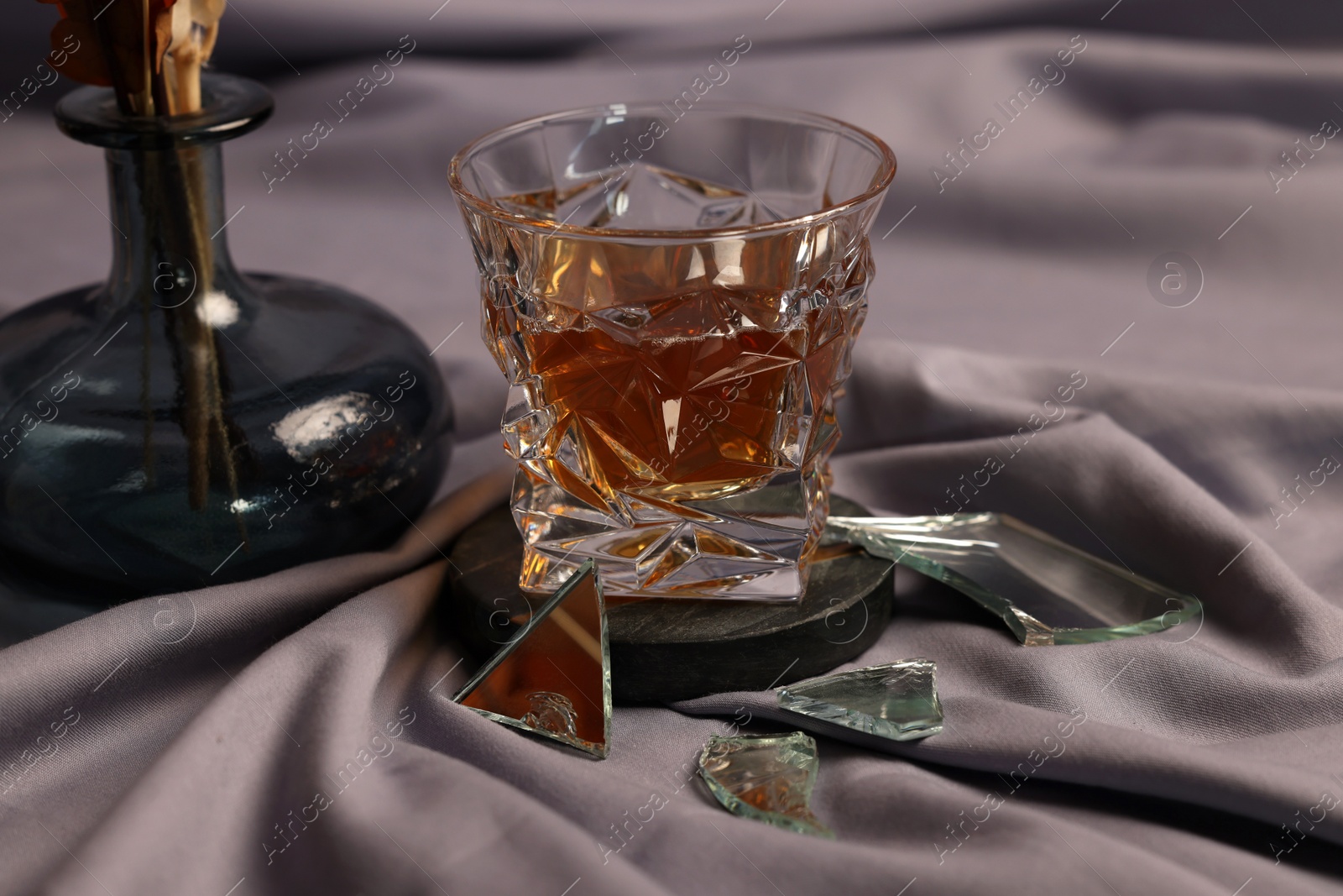 Photo of Glass of tasty alcohol drink and shards of broken mirror on grey fabric