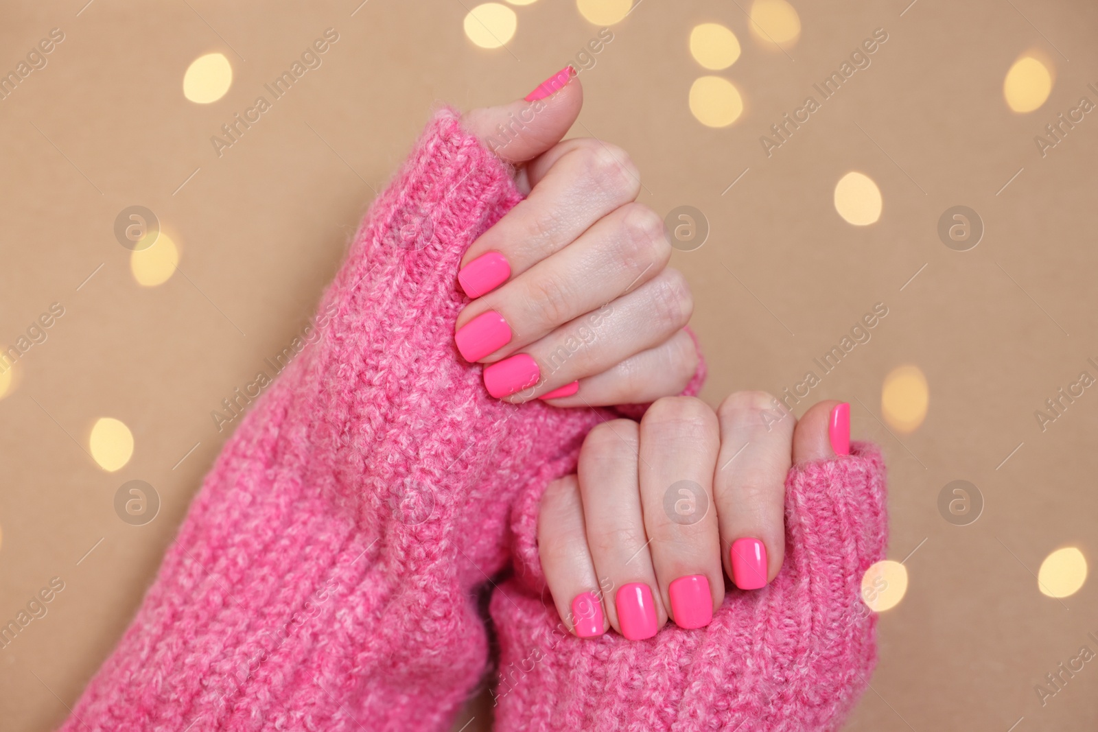 Photo of Woman showing her manicured hands with pink nail polish on dark beige background, top view. Bokeh effect