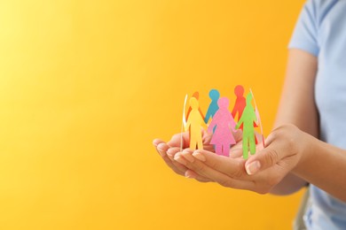 Photo of Woman holding paper human figures on yellow background, closeup with space for text. Diversity and inclusion concept