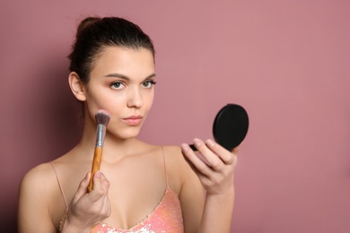 Photo of Young woman applying makeup on color background. Professional cosmetic products