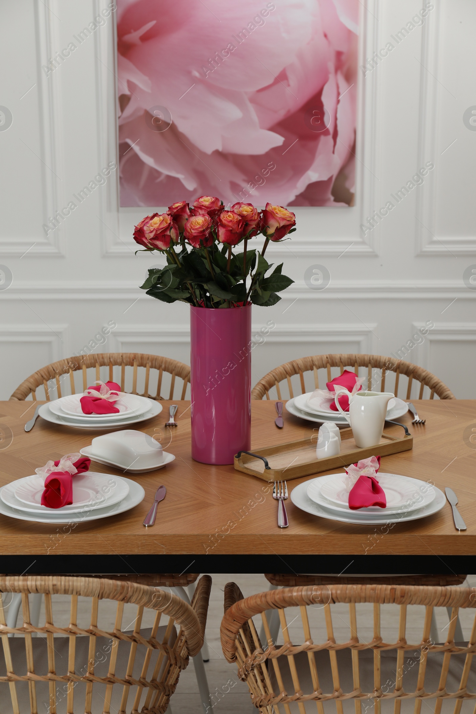 Photo of Color accent table setting. Plates, cutlery, pink napkins and vase with beautiful roses in dining room