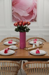 Color accent table setting. Plates, cutlery, pink napkins and vase with beautiful roses in dining room