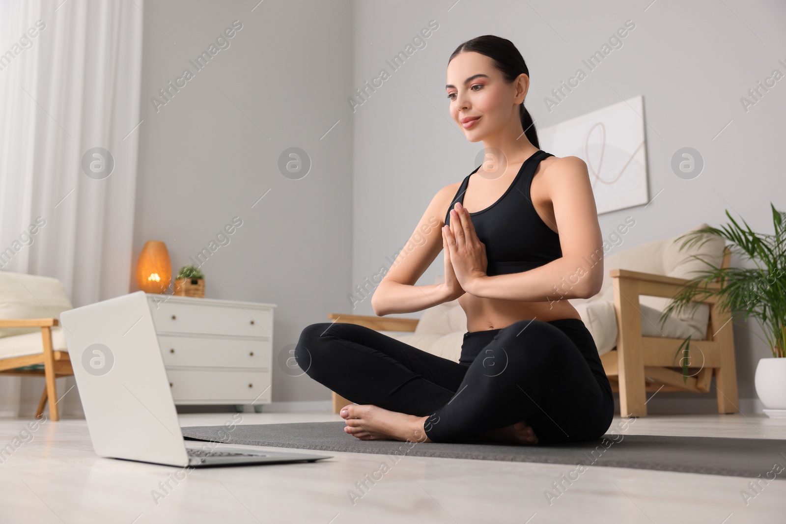 Photo of Beautiful young woman practicing Padmasana while watching online class on yoga mat at home, low angle view. Lotus pose