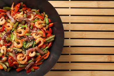 Photo of Shrimp stir fry with vegetables in wok on wooden mat, top view. Space for text
