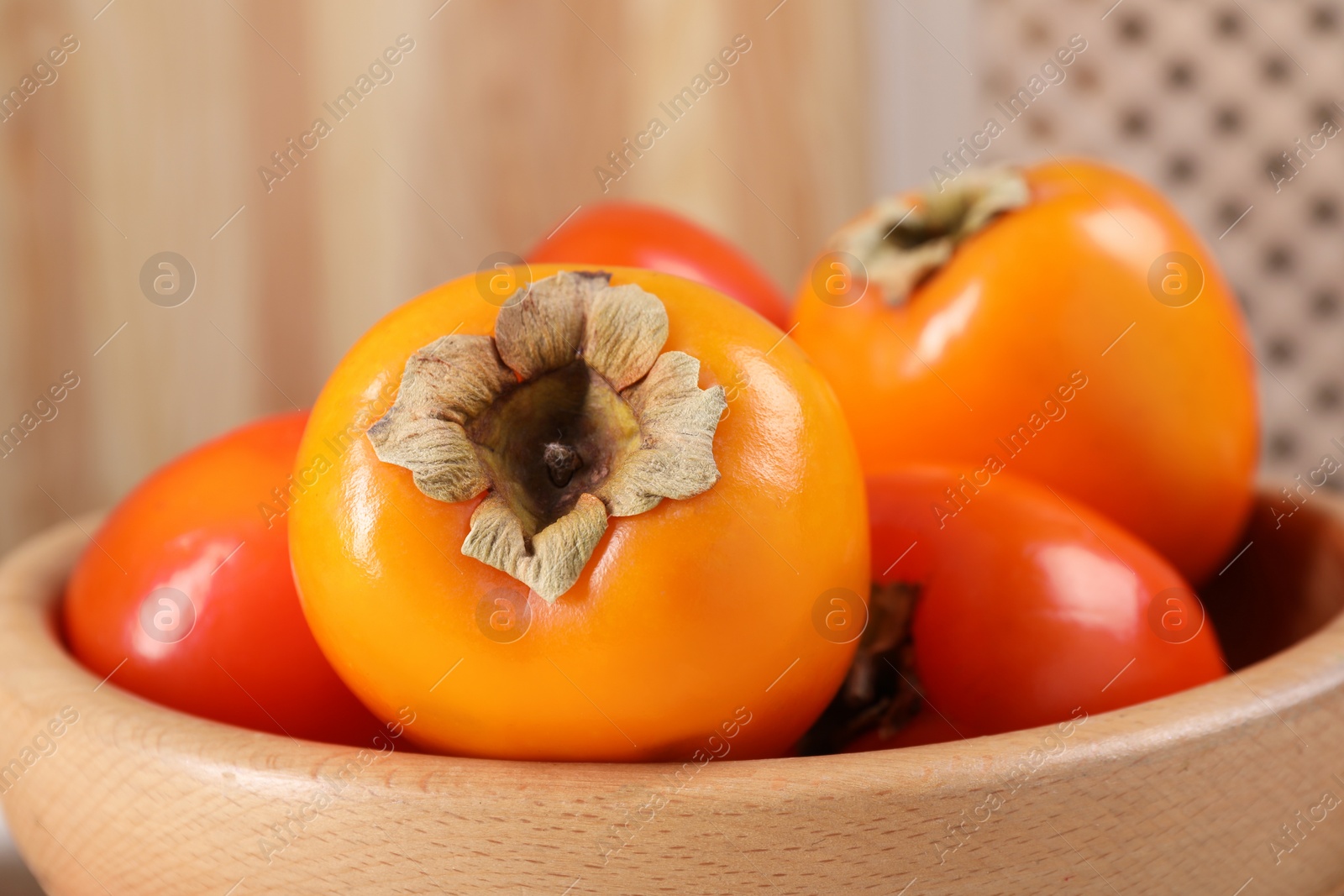 Photo of Delicious ripe persimmons in bowl on blurred background, closeup