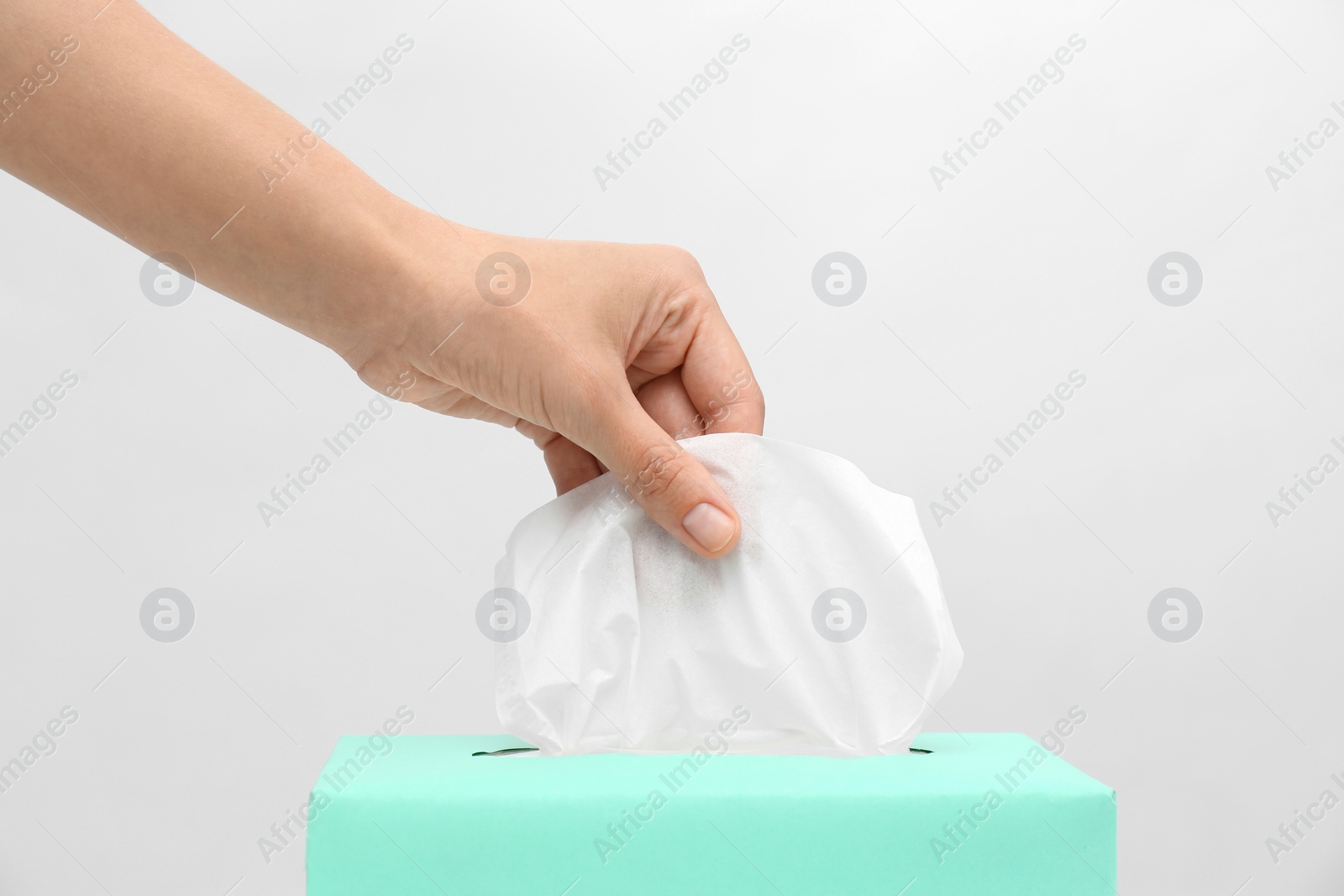 Photo of Woman taking paper tissue from box on light background, closeup