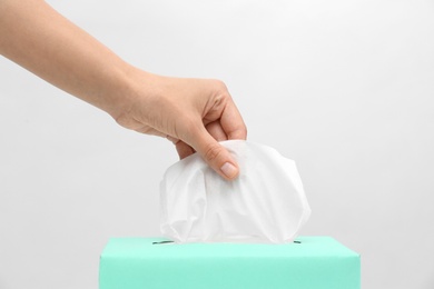 Woman taking paper tissue from box on light background, closeup