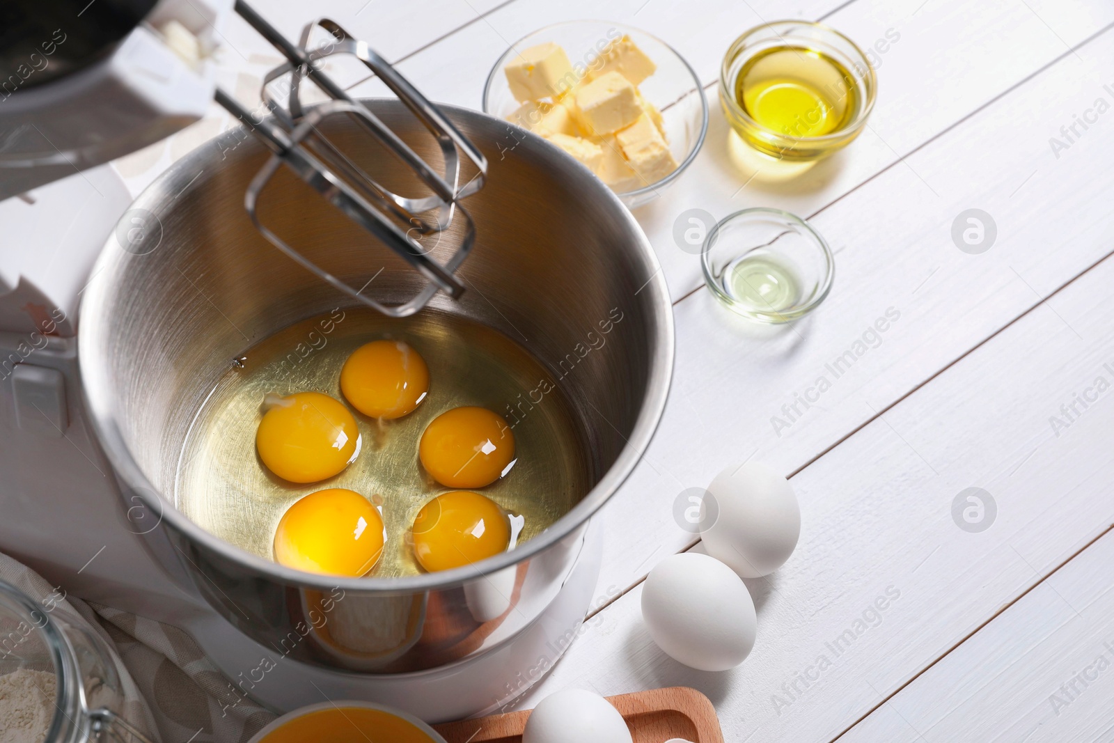 Photo of Making dough. Raw eggs in bowl of stand mixer and ingredients on white wooden table, space for text