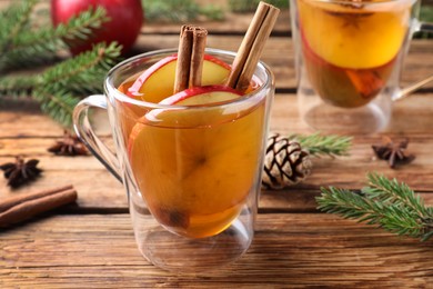 Photo of Hot mulled cider and fir branches on wooden table, closeup