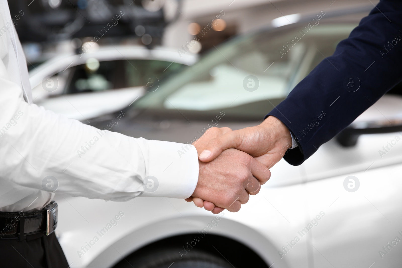 Photo of Young salesman shaking hands with client in car dealership