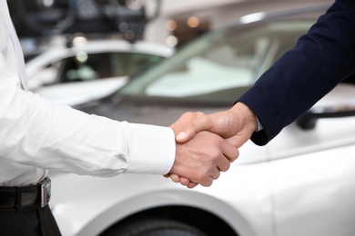 Young salesman shaking hands with client in car dealership