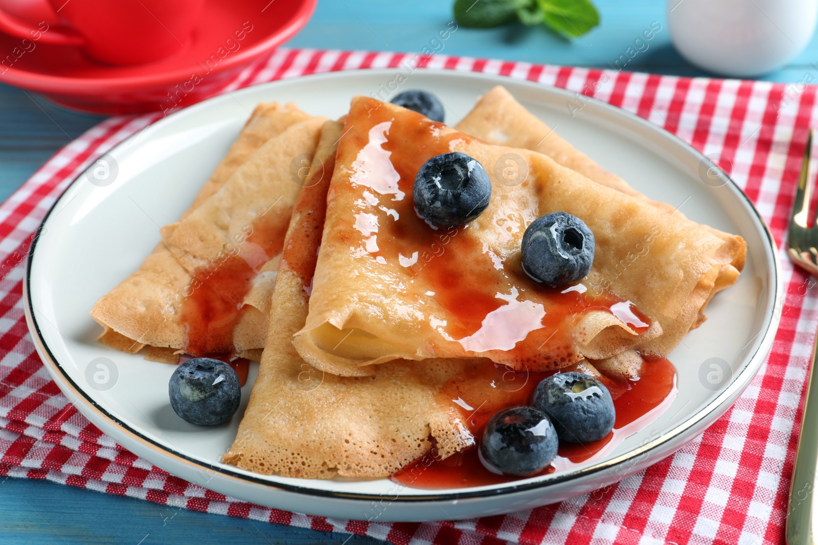 Photo of Delicious crepes served with blueberries and syrup on table, closeup