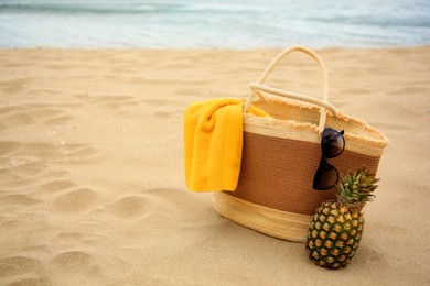 Photo of Straw bag with towel, sunglasses and fresh pineapple on beach, space for text