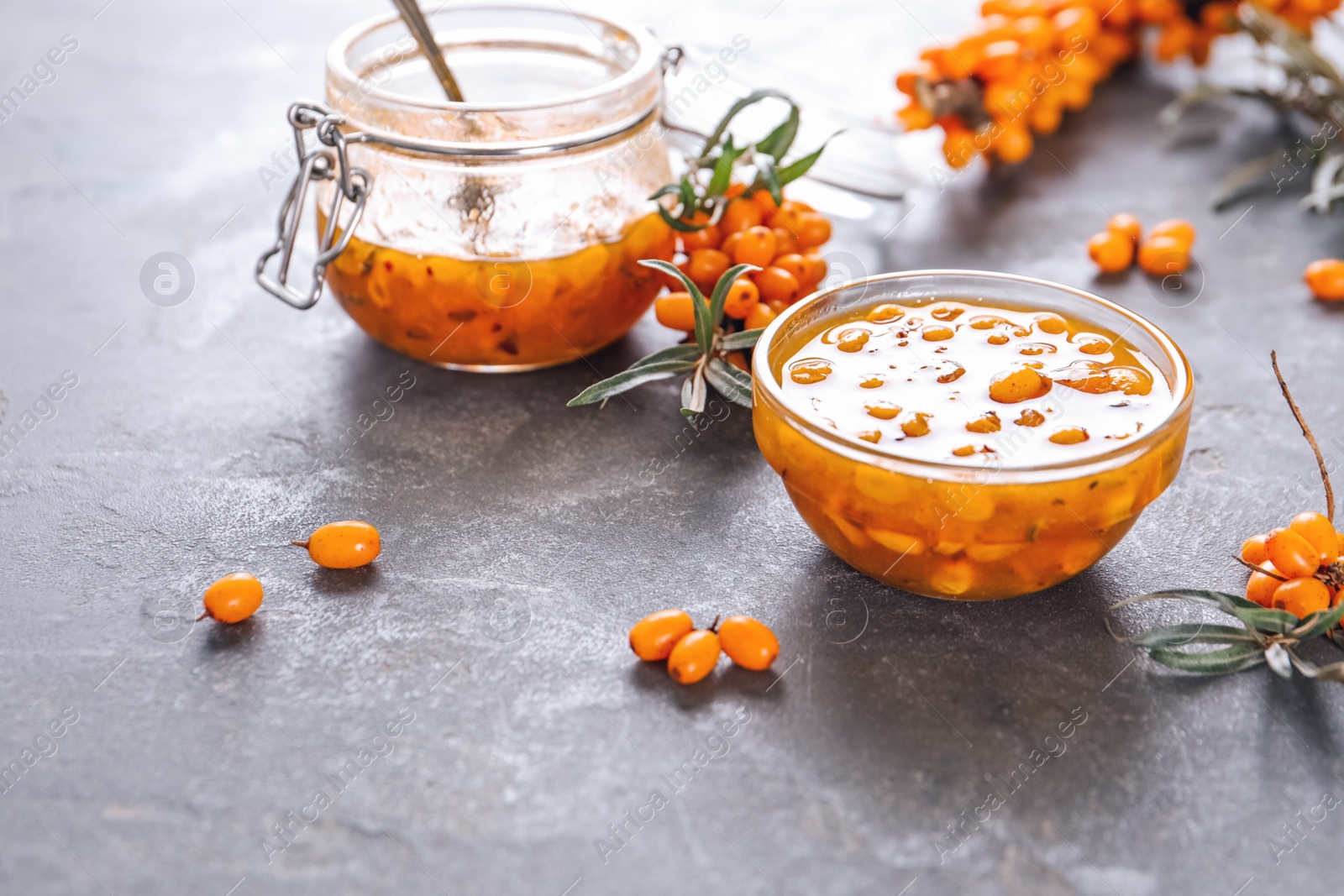 Photo of Delicious sea buckthorn jam and fresh berries on grey table. Space for text