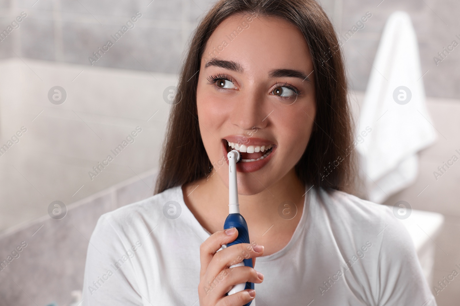 Photo of Young woman brushing her teeth with electric toothbrush in bathroom