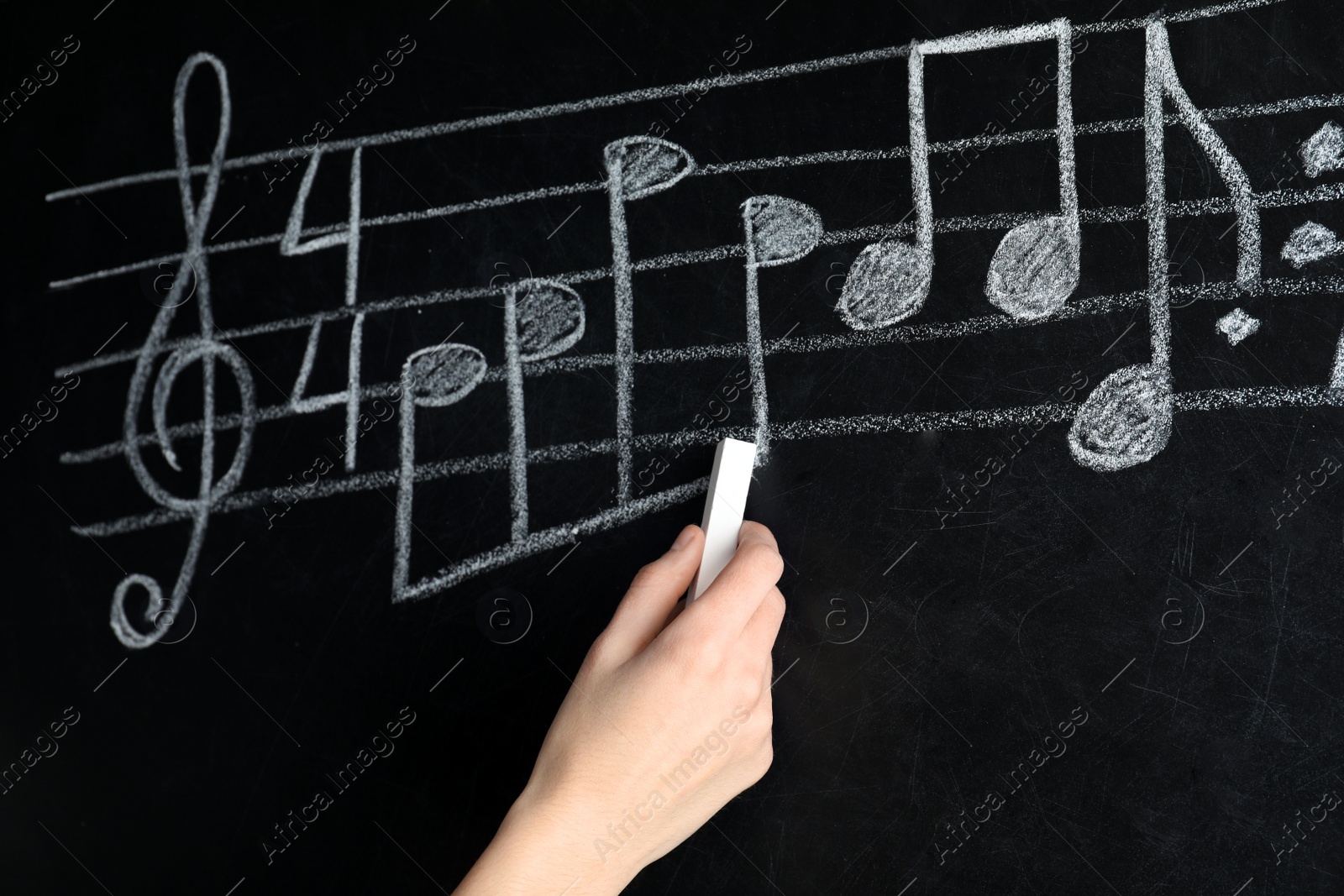 Photo of Woman writing music notes with chalk on blackboard, closeup