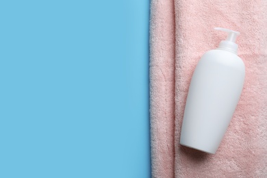 Bottle of shampoo and towel on color background, top view with space for text