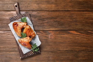Photo of Delicious fried chicken wings on wooden table, top view. Space for text