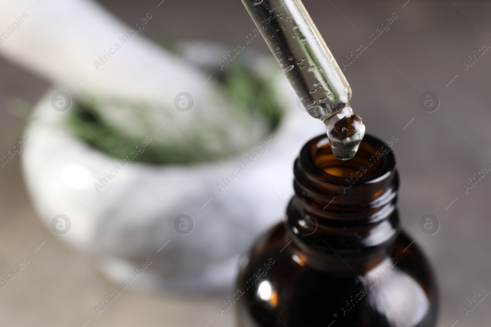 Photo of Dripping dill essential oil from pipette into bottle on blurred background, closeup. Space for text