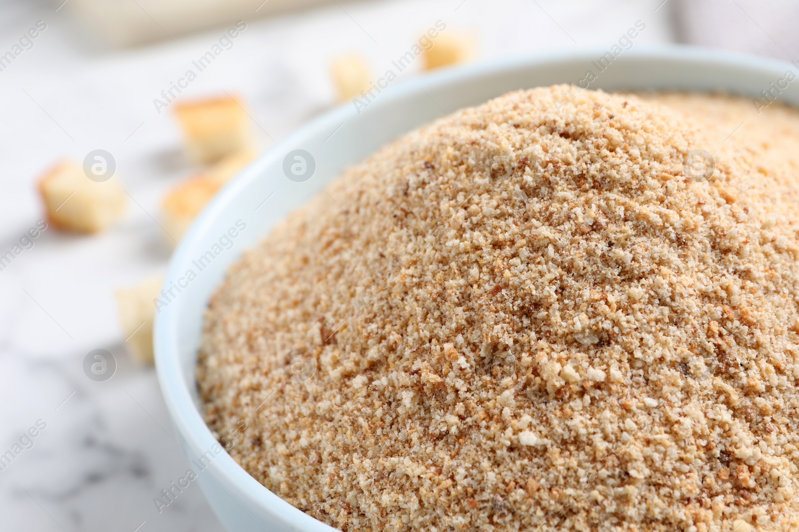 Photo of Fresh breadcrumbs in bowl on white marble table, closeup