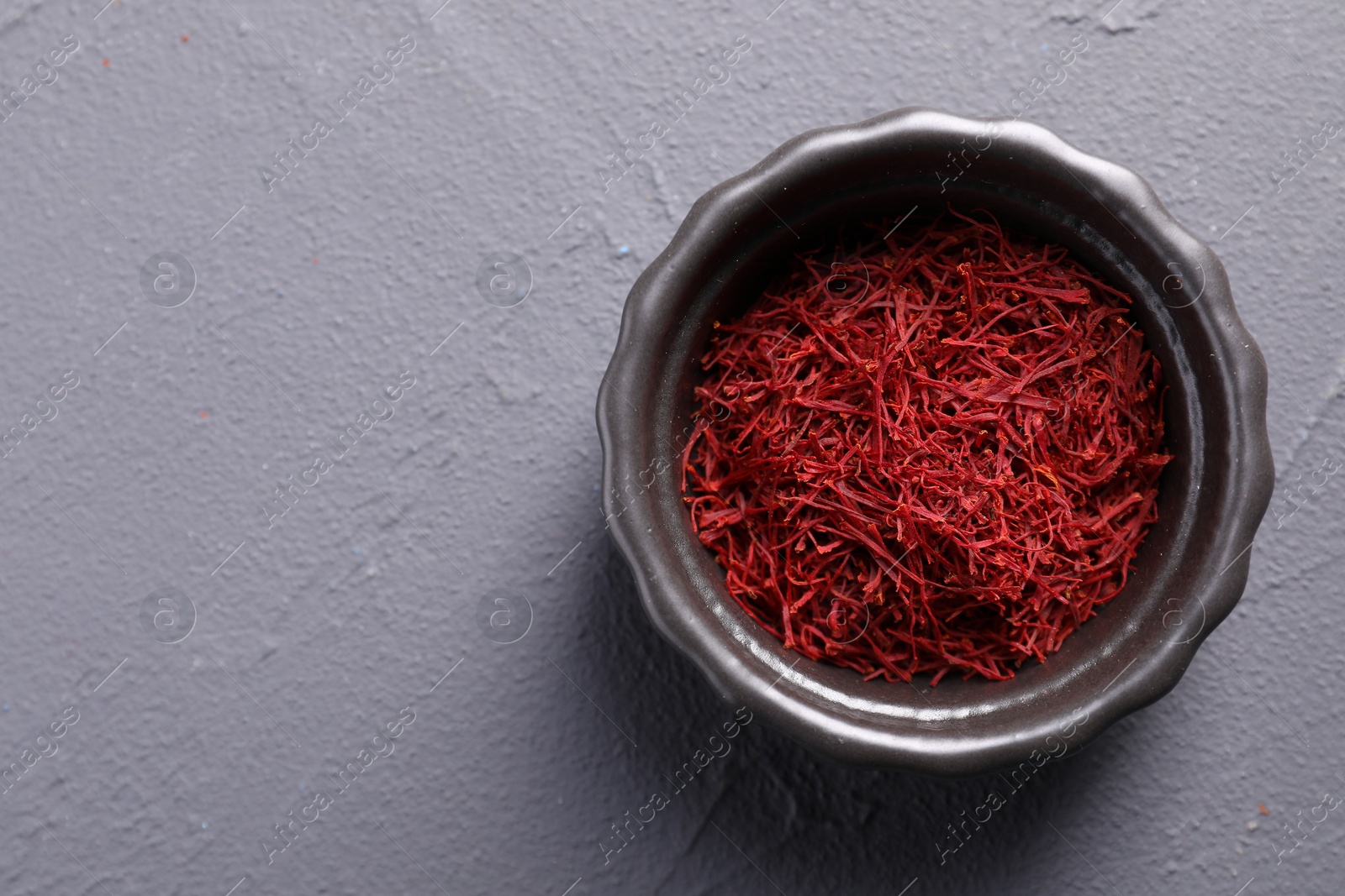 Photo of Aromatic saffron in bowl on gray table, top view. Space for text