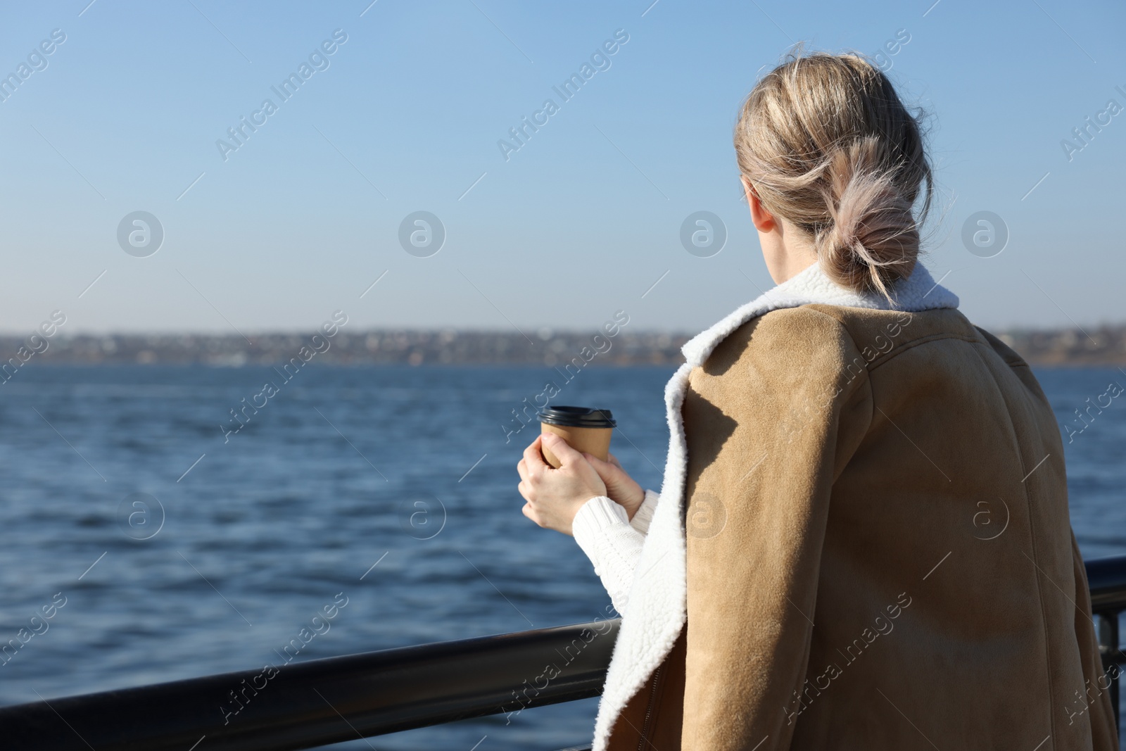 Photo of Lonely woman with cup of drink near river on sunny day, back view