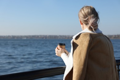 Photo of Lonely woman with cup of drink near river on sunny day, back view