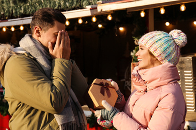 Photo of Young woman presenting Christmas gift to her boyfriend at winter fair