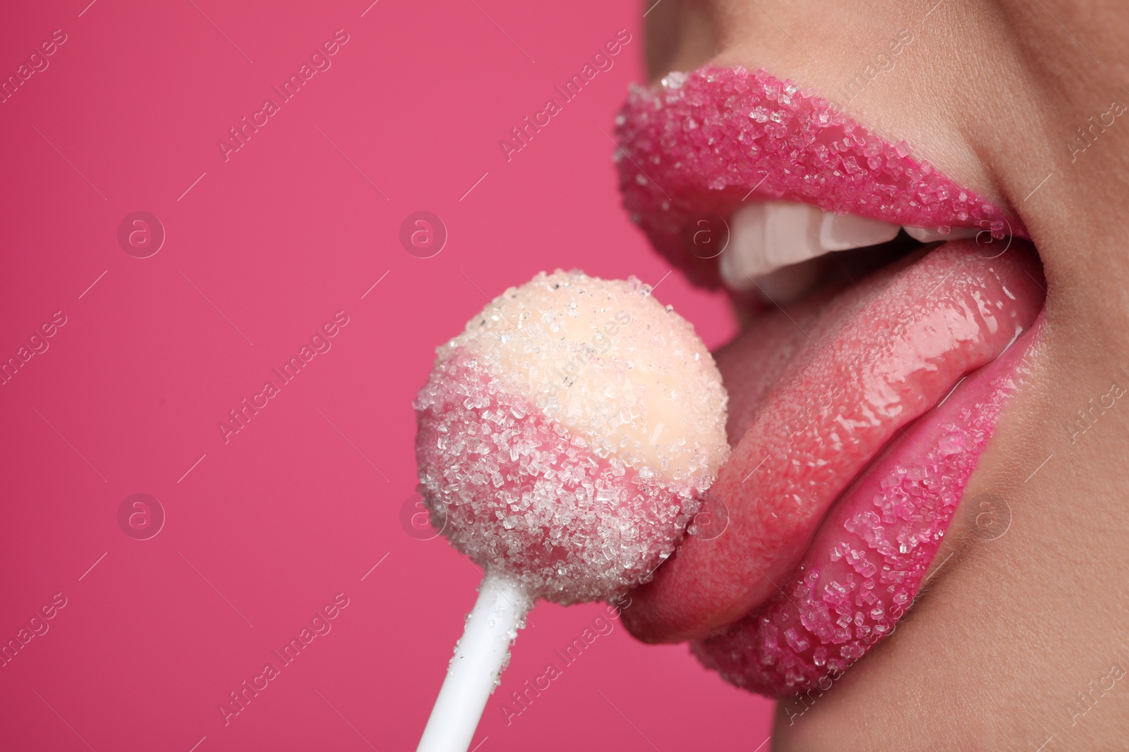 Photo of Young woman with beautiful lips covered in sugar eating lollipop on pink background, closeup