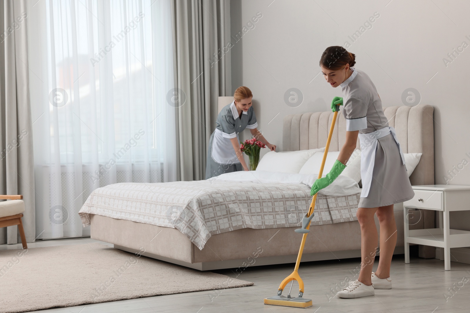 Photo of Professional chambermaids cleaning up bedroom in hotel