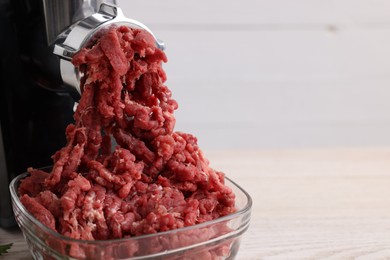 Photo of Electric meat grinder with beef mince on table, closeup. Space for text
