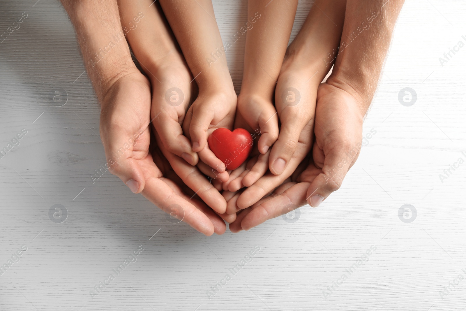 Photo of Family holding small red heart in hands on wooden background