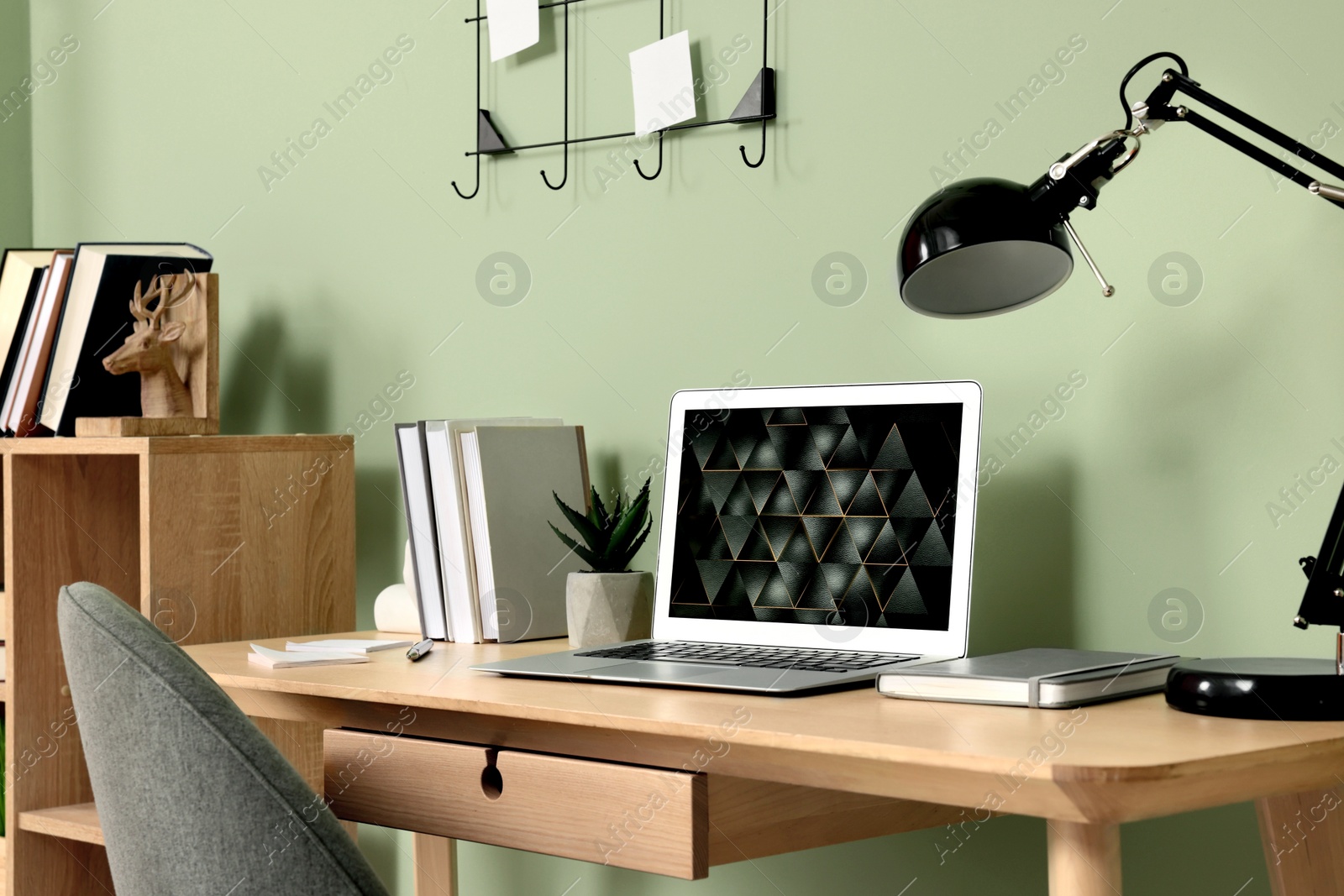 Photo of Modern laptop, books, lamp and stationery on wooden desk near green wall. Home office