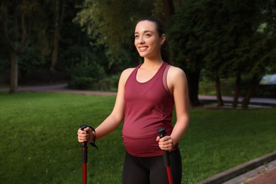 Pregnant woman practicing Nordic walking with poles outdoors