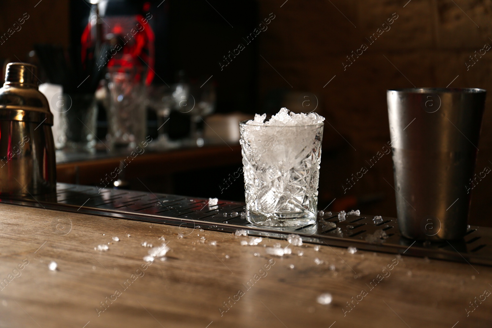 Photo of Glass with ice on bar counter, space for text. Preparing alcoholic cocktail