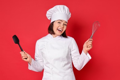 Photo of Happy confectioner holding whisk and spatula on red background