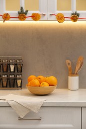 Photo of Handmade garland from dry orange slices and fir branches hanging on cabinets in kitchen