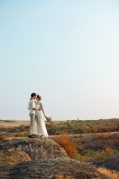 Happy newlyweds with beautiful field bouquet outdoors