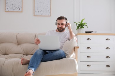 Man with laptop and headphones sitting on sofa at home