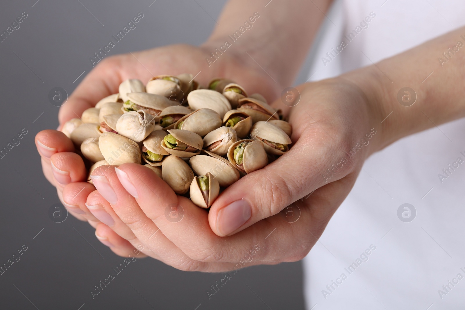 Photo of Woman holding handful of tasty pistachios on grey background, closeup