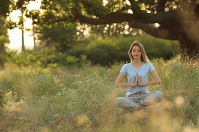 Young woman meditating on green grass in park, space for text