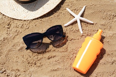 Photo of Blank bottle of sunscreen, starfish and beach accessories on sand, above view