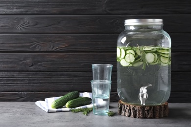 Photo of Composition with jar dispenser of fresh cucumber water on table against dark background. Space for text