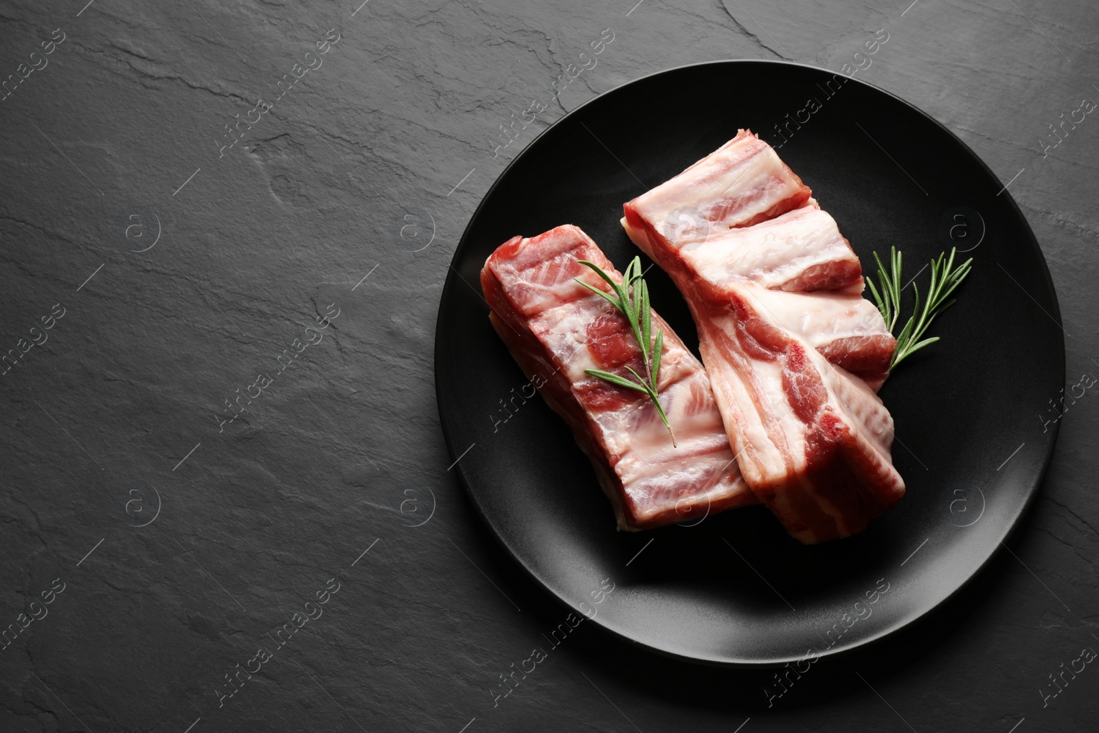 Photo of Raw ribs with rosemary on black table, top view