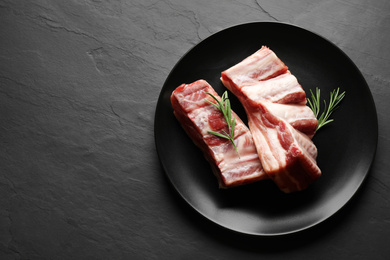 Raw ribs with rosemary on black table, top view