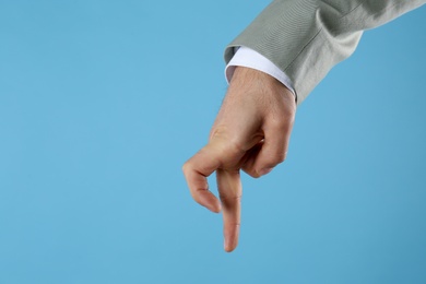 Photo of Businessman imitating walk with hand on light blue background, closeup. Finger gesture